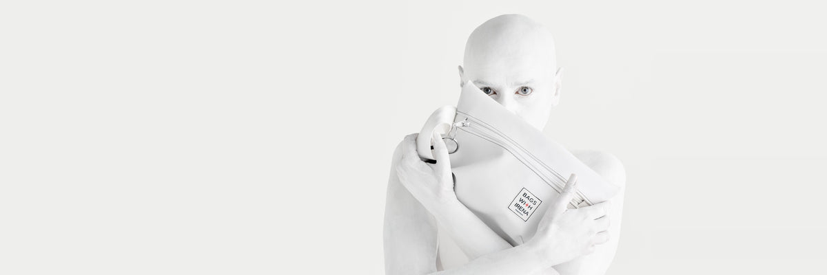 Die Künstlerin Irena Pejčić, ganz in Weiß bemalt, hält eine weiße Tasche mit dem Label Bags With Irena vor ihr Gesicht