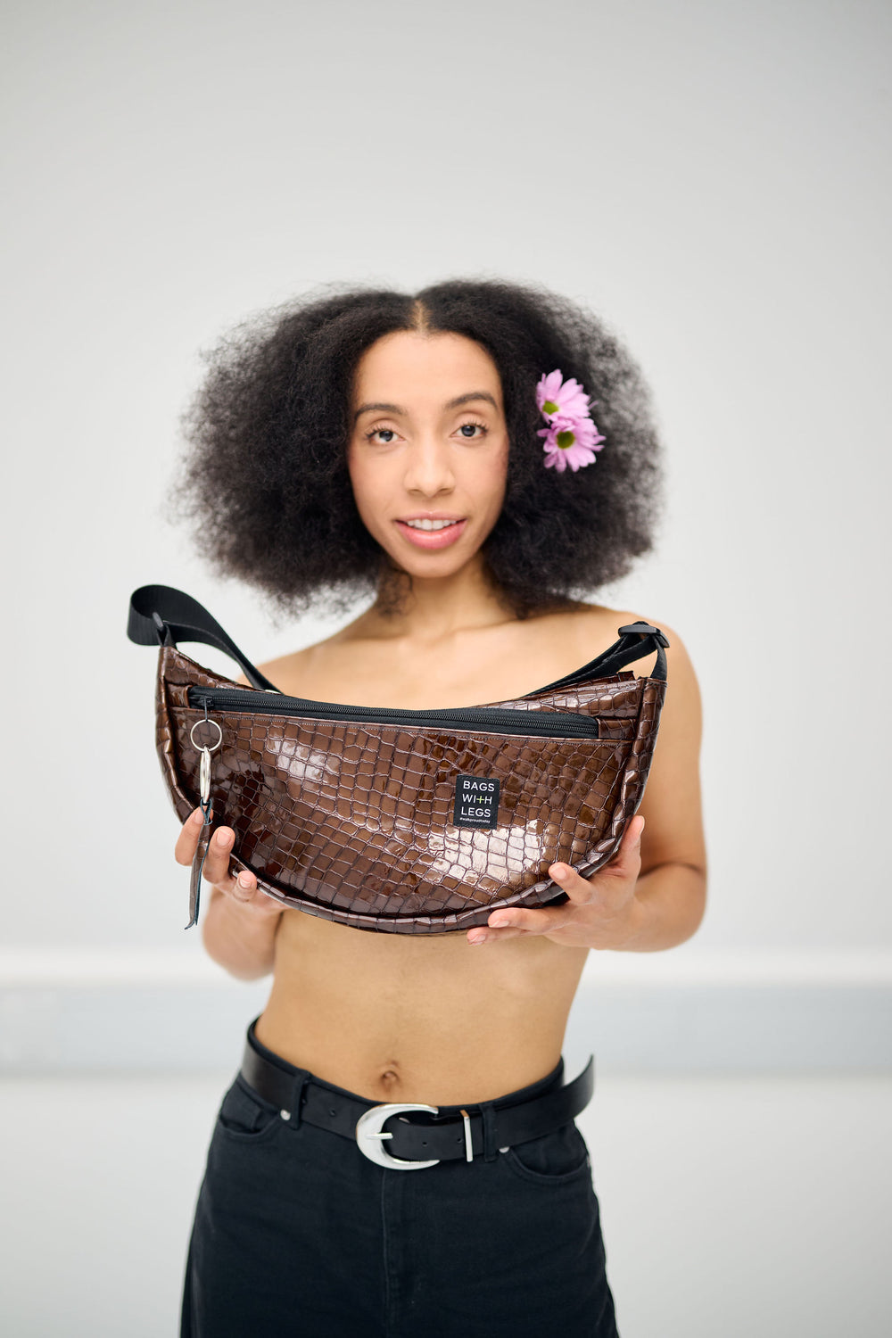 Ruby Love Moonwalker Bag in Kroko-Optik, vor der Brust gehalten, mit Blüten im Haar