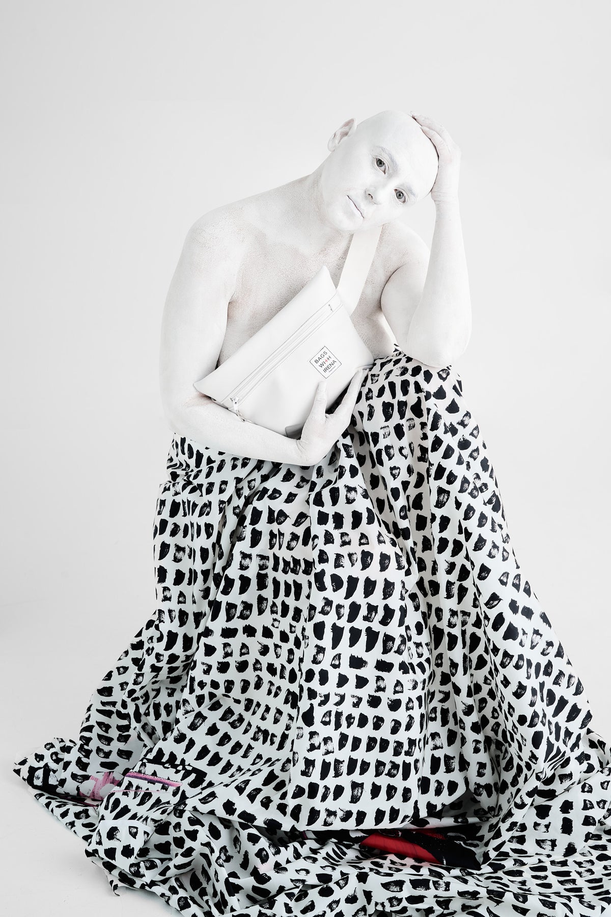 Artist Irena Pejčić, painted white from head to toe, sits wrapped in black and white fabric, holding a bag2back bag