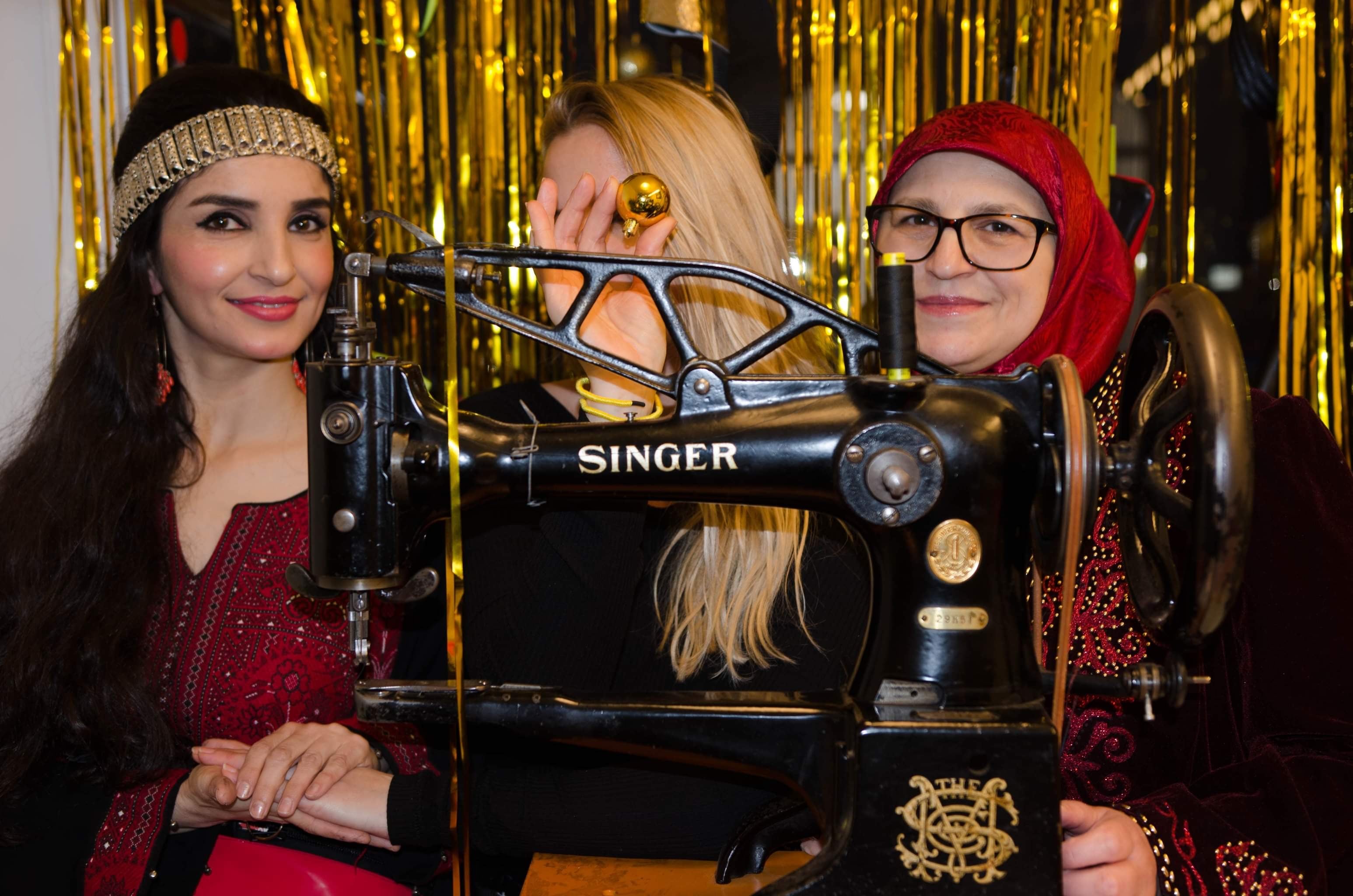 Drei Macherinnen von Bags With Legs an einer alten Singer-Nähmaschine vor goldenem Hintergrund