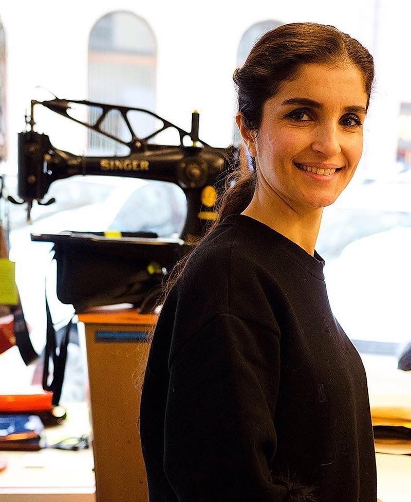 Asilla Wase lächelt neben einer Singer-Nähmaschine im Atelier